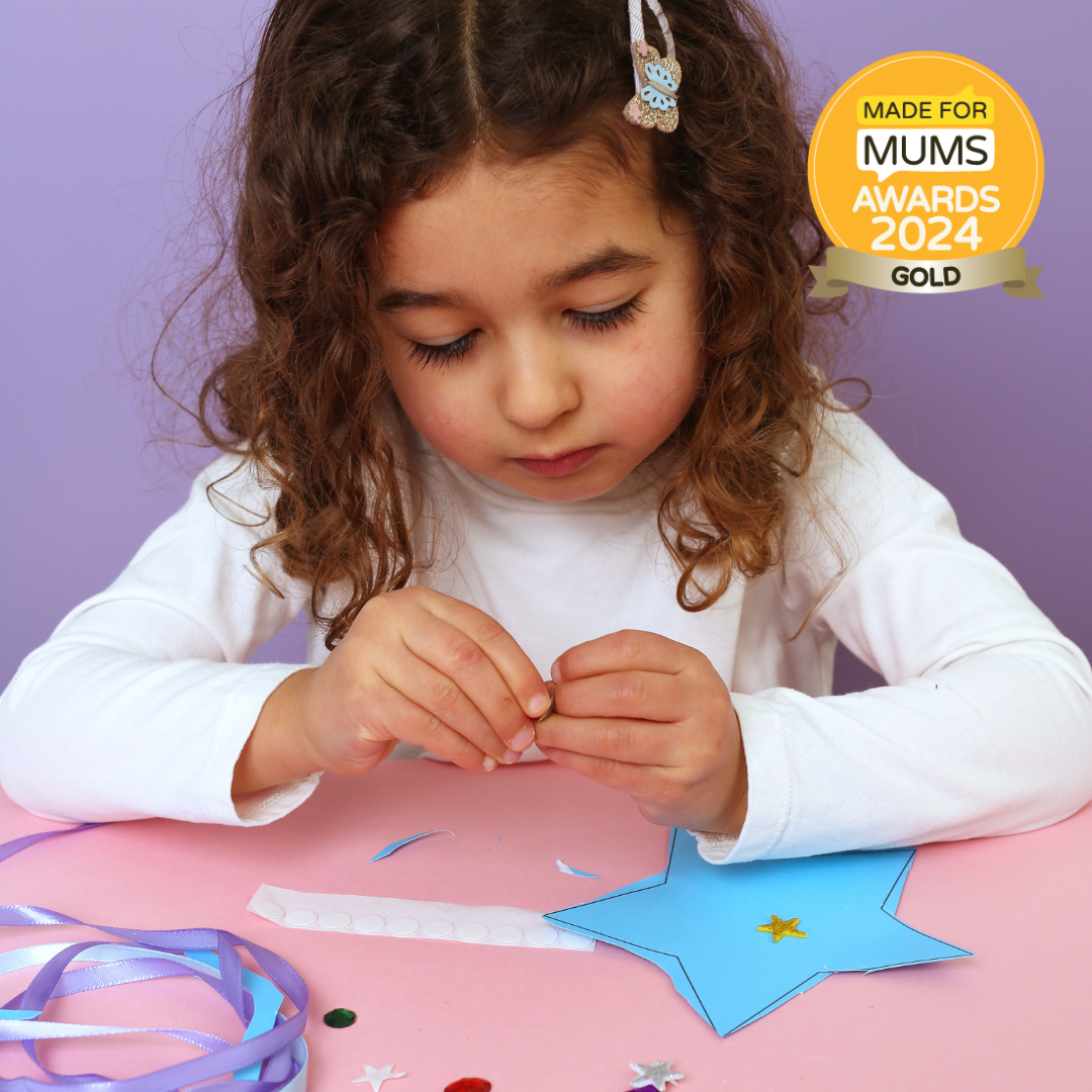Child engaged in craft activity with decorative items on a pink table, against a purple background, with 'Made for Mums Awards 2024 Gold' badge.