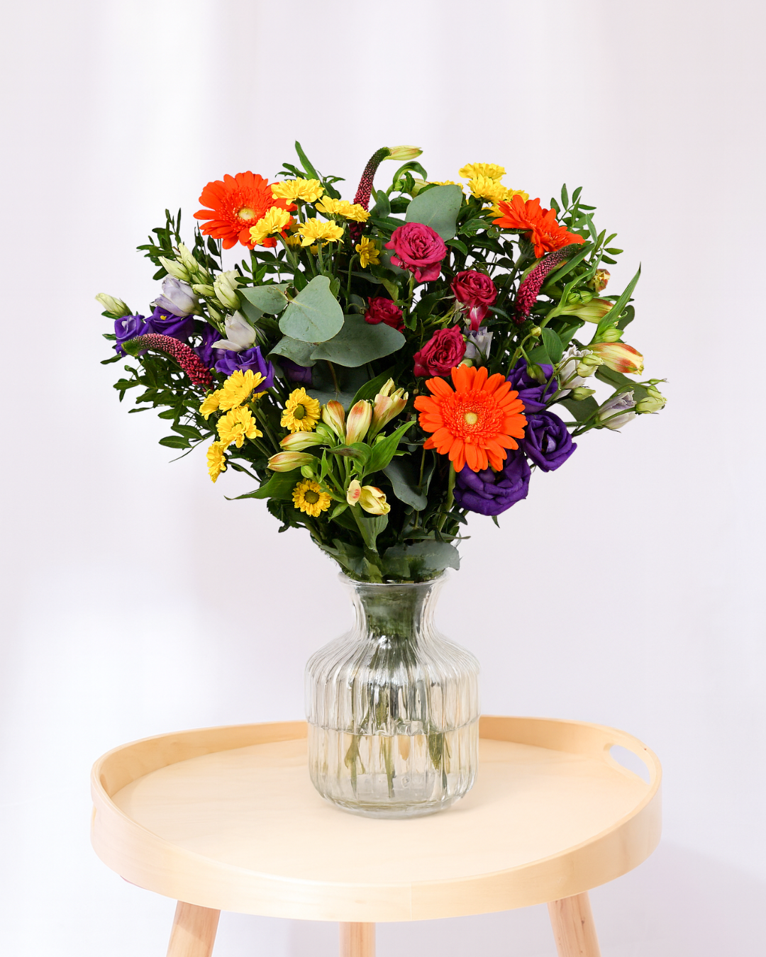 Colorful bouquet of flowers in a clear vase on a wooden table with a white background