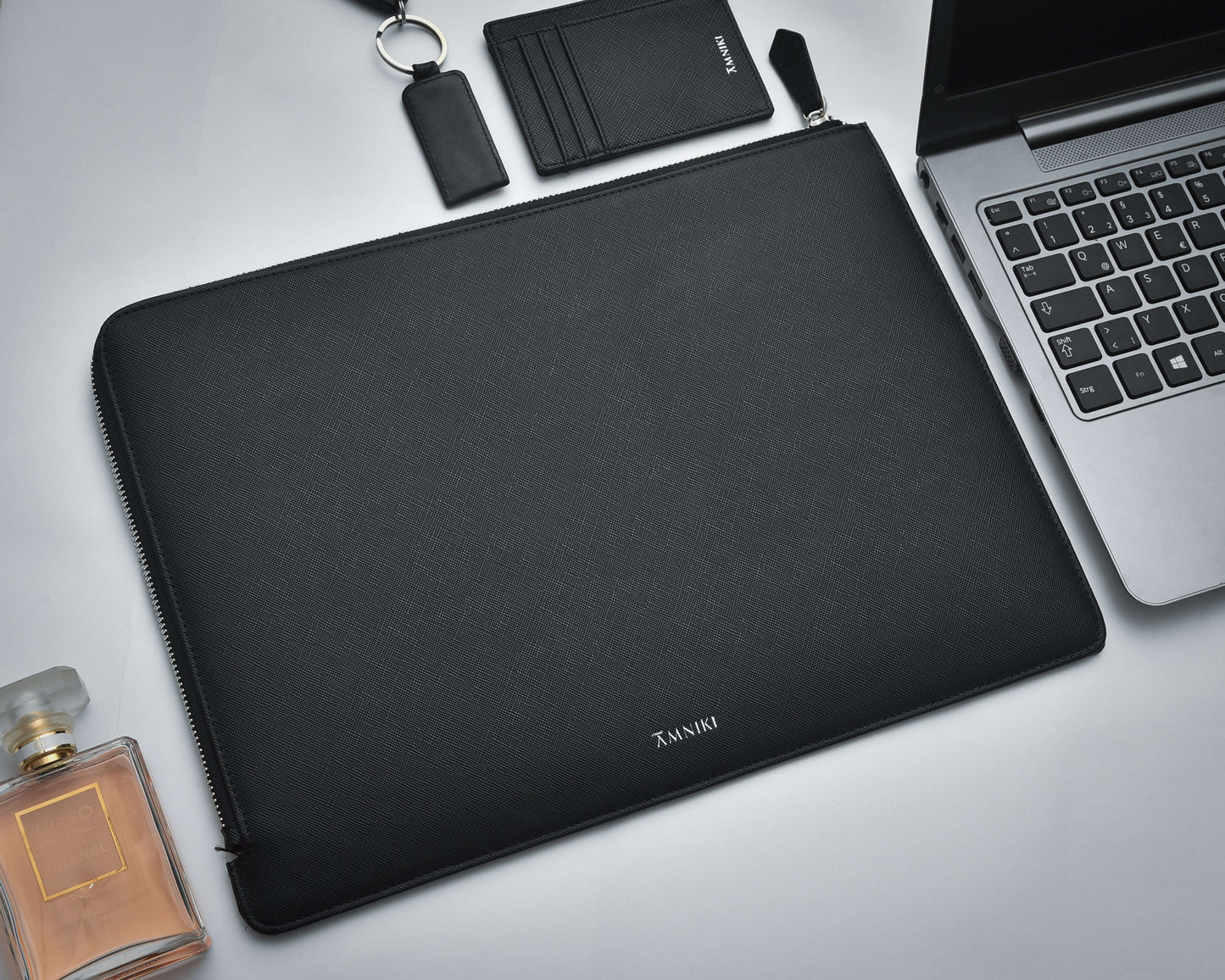 Black laptop sleeve with a laptop, perfume bottle, and wallet on a light gray background