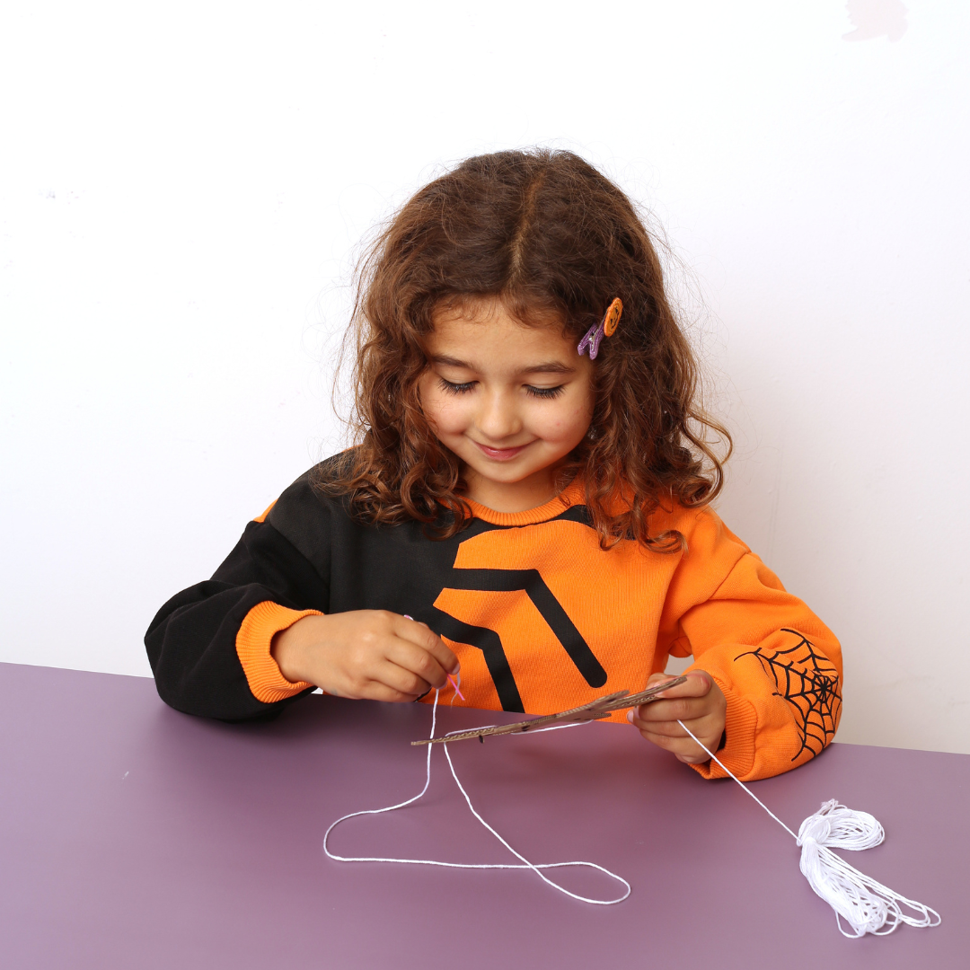 Child in orange and black shirt with spider design cutting string on purple table