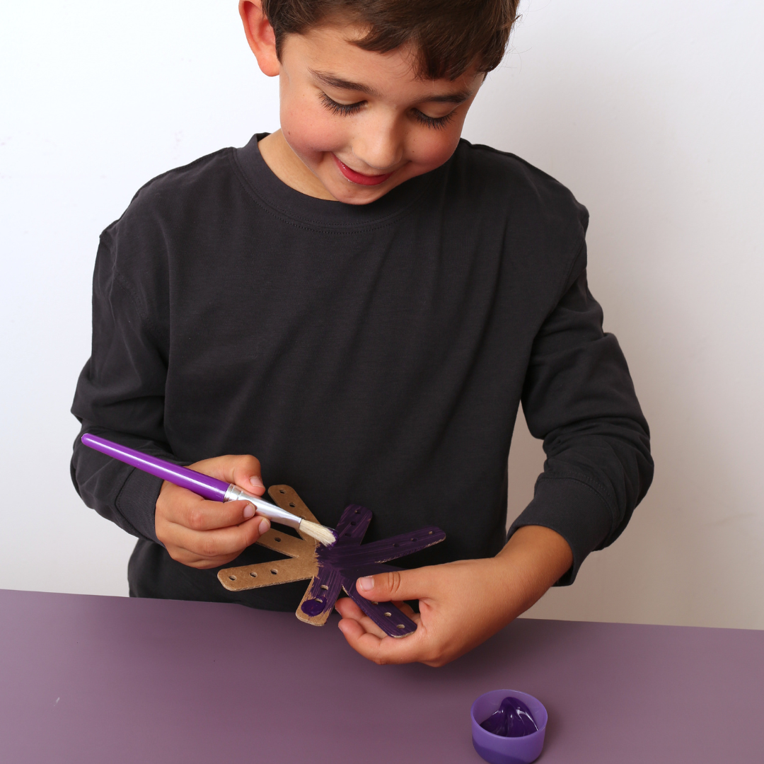 Child painting a purple object with a brush on a white background