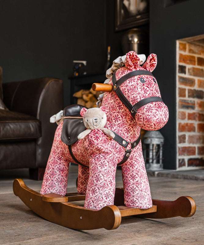 Pink patterned rocking horse with a teddy bear in a living room setting.