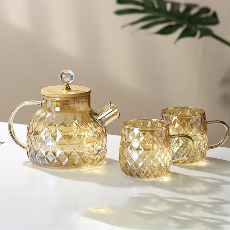 Glass teapot and two mugs with diamond cut design on a light surface.