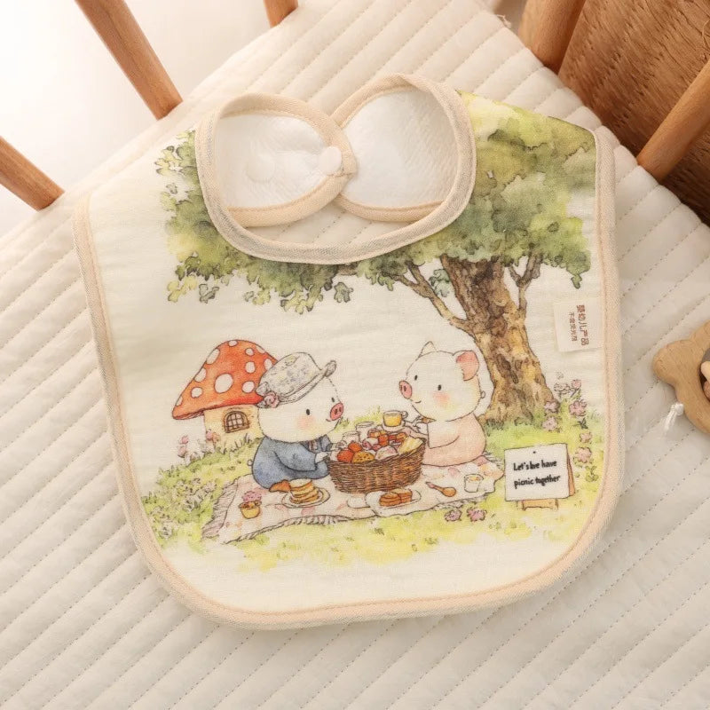 Baby bib with cartoon design of two animals having a picnic, placed on a quilted surface.