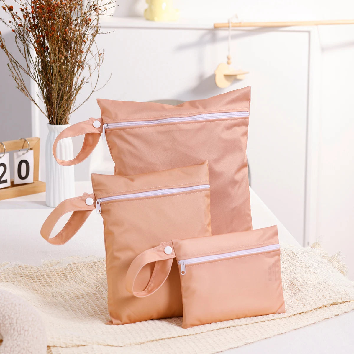 Set of peach-colored reusable nappy bags with zippers on a white surface.