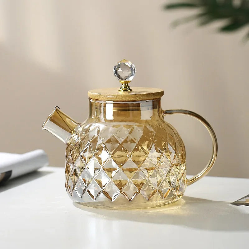 Glass teapot with diamond pattern and wooden lid on a light surface.