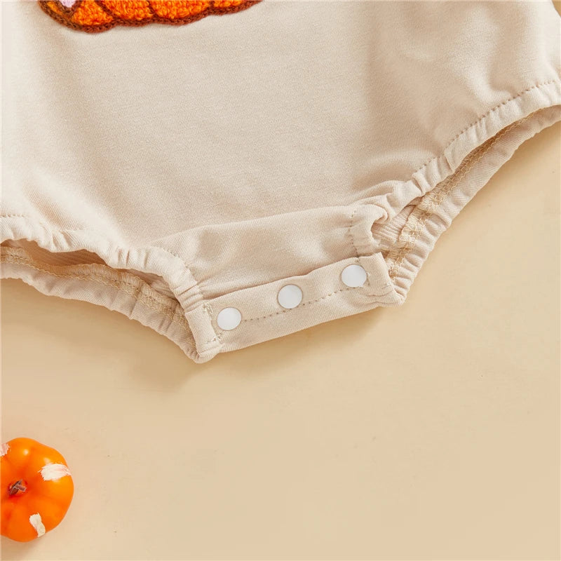 Beige baby romper with white buttons on a beige background with small pumpkins.