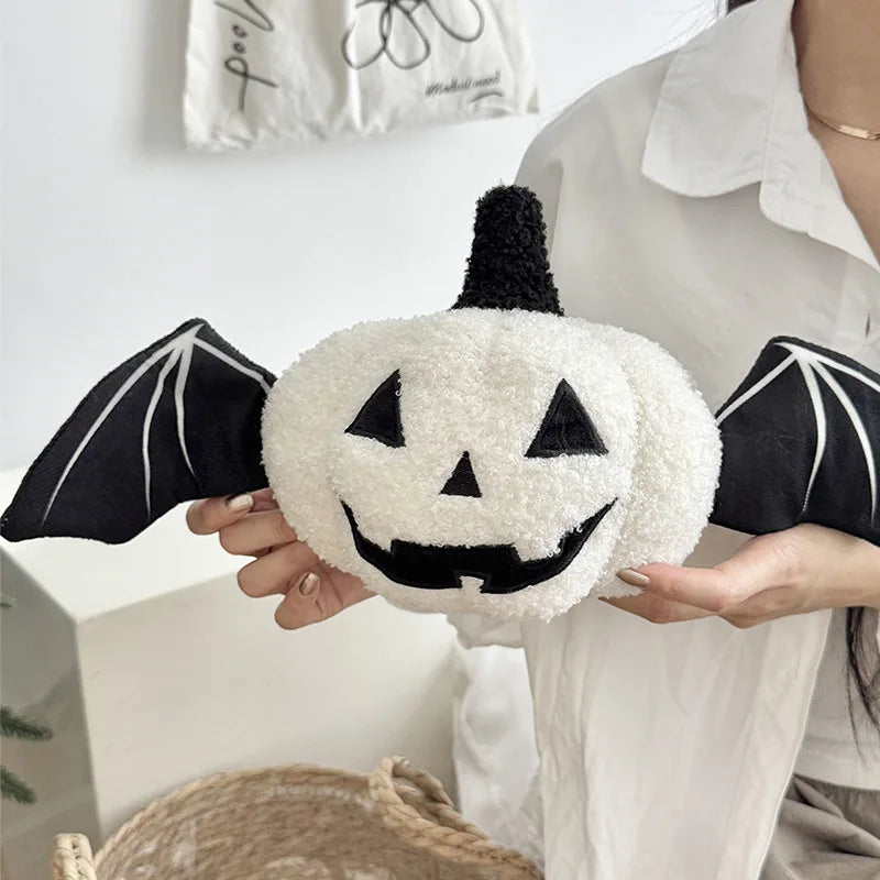 Person holding a Halloween-themed plush toy with a pumpkin face, bat wings, and a black top.