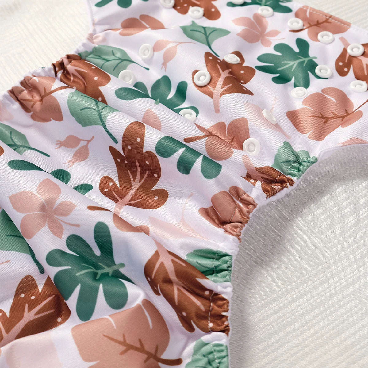 Floral patterned reusable nappy with brown, green, and pink leaves on a white background.