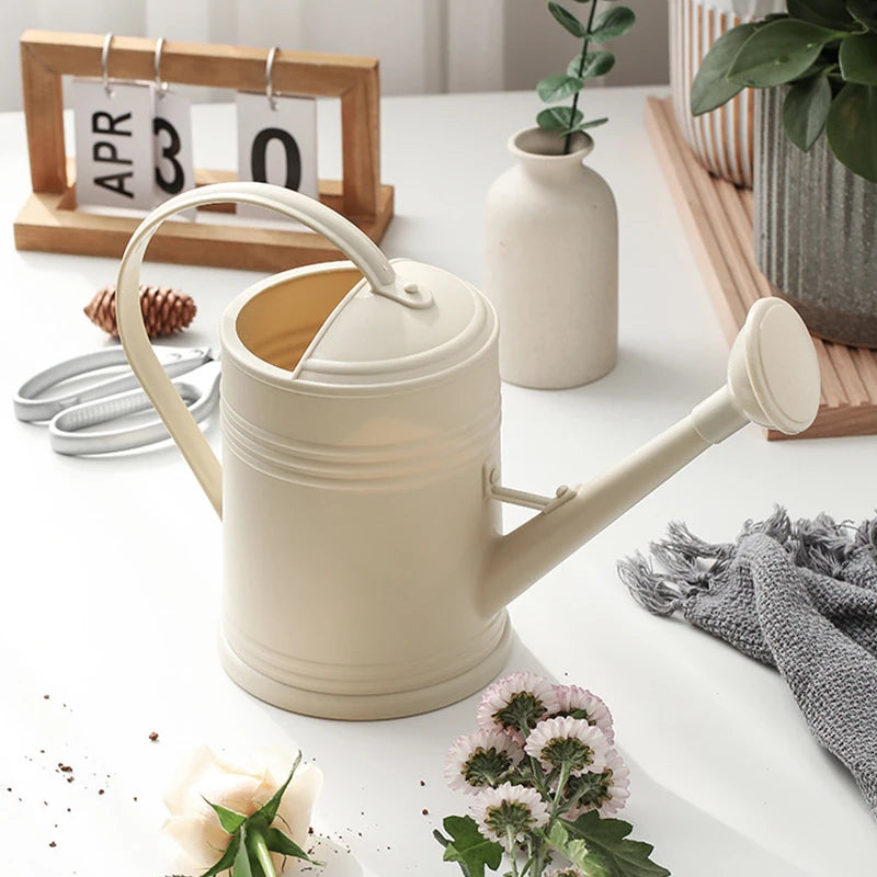 Beige watering can on a table with plants and decor items