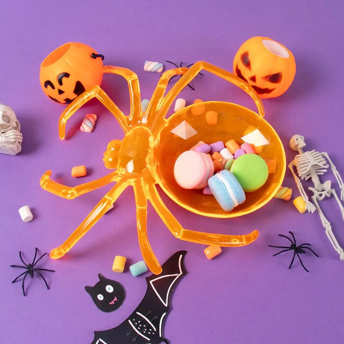 Spider-shaped bowl filled with colorful candies on a purple background with Halloween decorations.