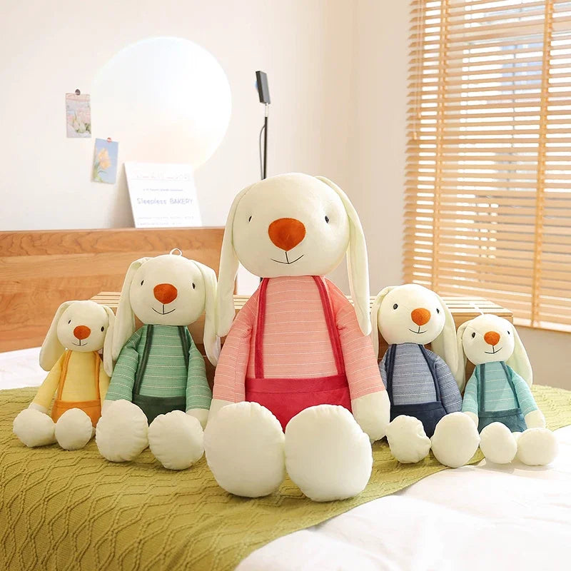 Five plush rabbit toys of different colors sitting on a bed.