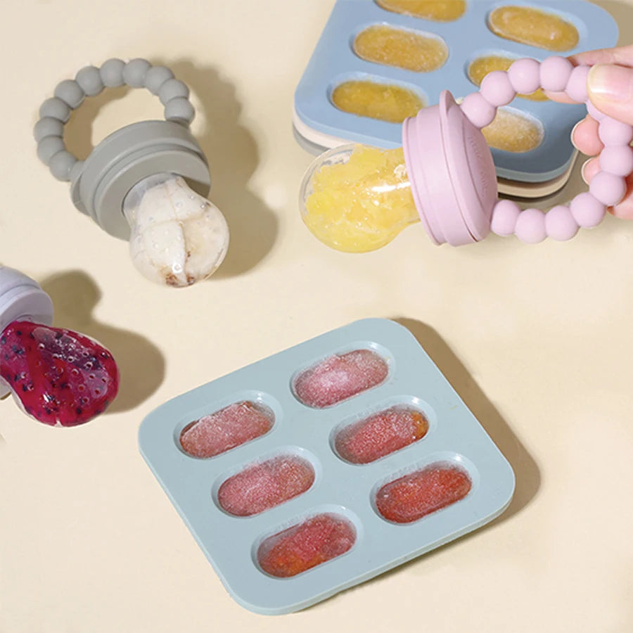 Ice cube trays with frozen fruit puree and baby teethers on a beige background