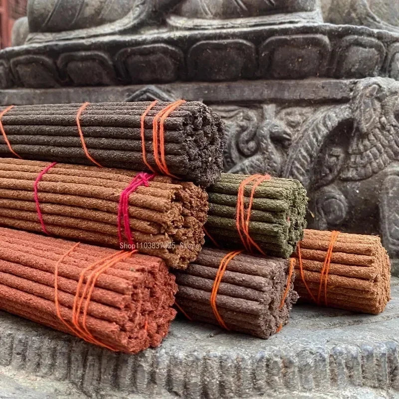Bundles of incense sticks tied with orange and red strings on a stone surface with a stone sculpture in the background.