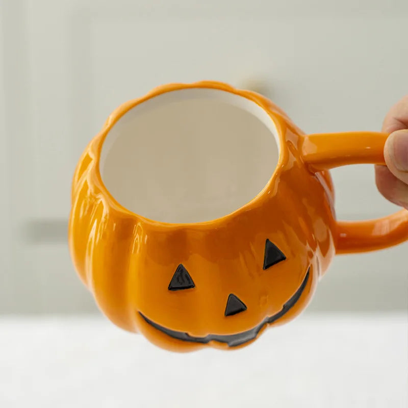 Orange pumpkin-shaped mug with a face design held by a hand against a light background