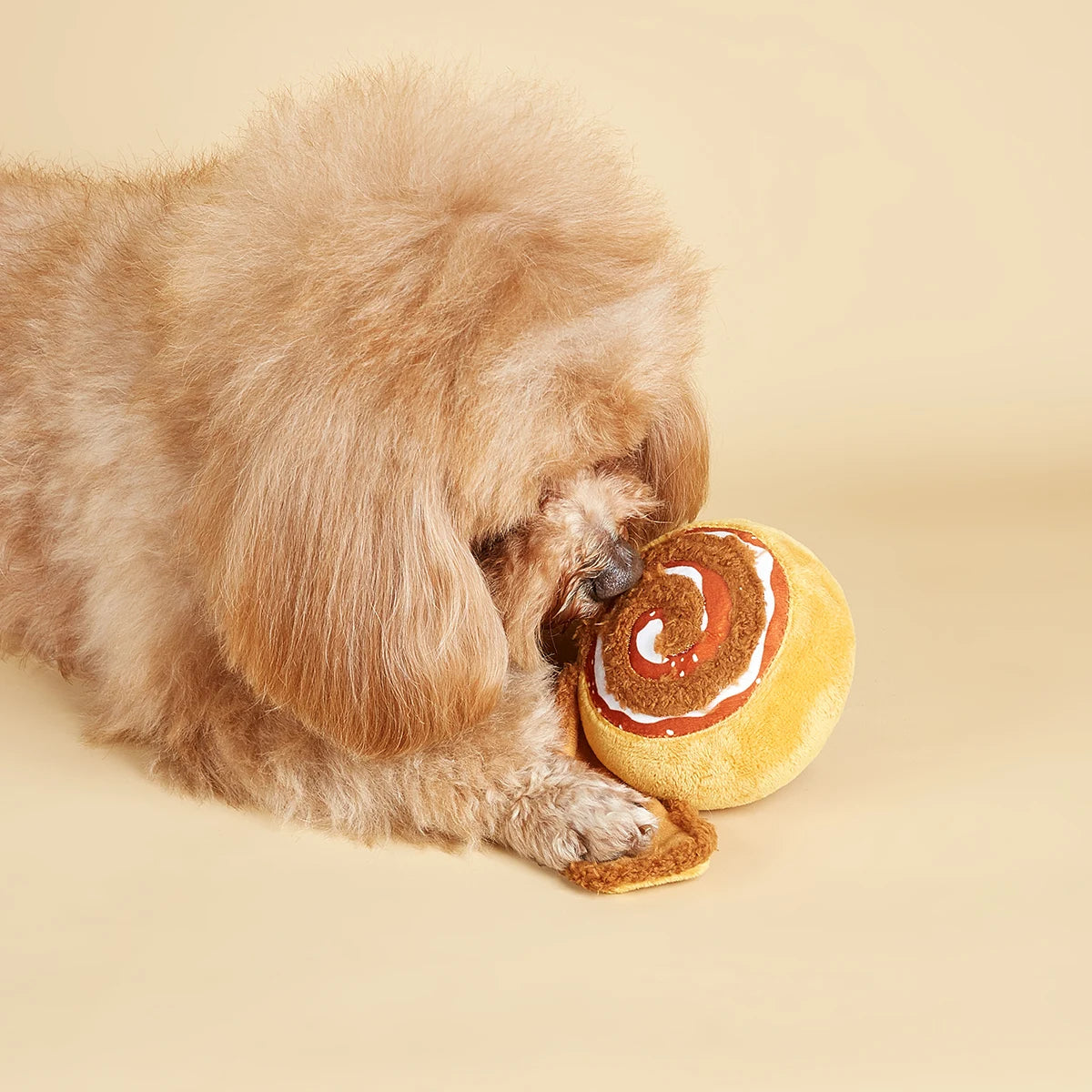 Dog playing with a toy resembling a cinnamon roll on a beige background