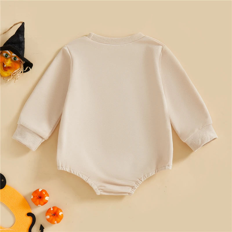 White baby onesie on a beige background with Halloween decorations.