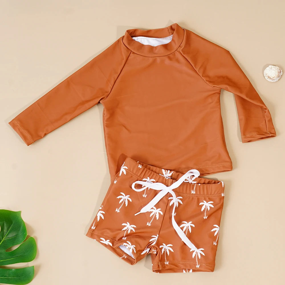 Orange long-sleeve rash guard and swim shorts with palm tree pattern on a beige background