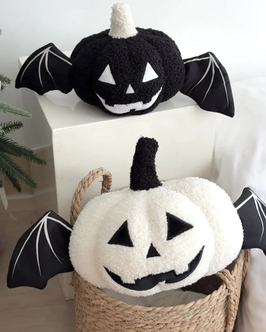 Two Halloween-themed plush toys shaped like pumpkins with bat wings on a white surface.