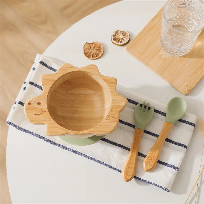 Wooden dinosaur-shaped bowl with green fork and spoon on a striped cloth, with lemon slices and a glass of water in the background.