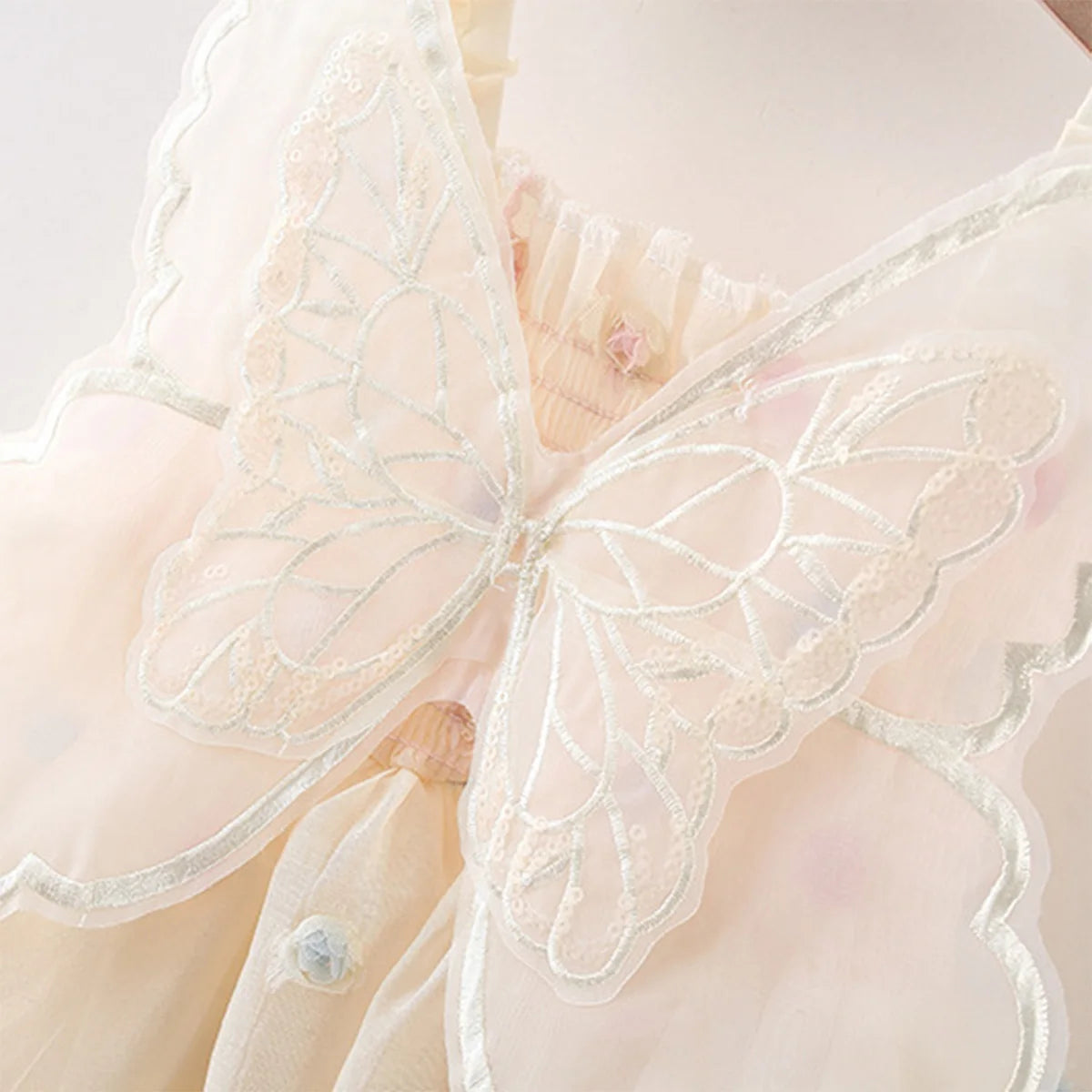 Close-up of a beige baby fairy dress with butterfly lace details on a white background