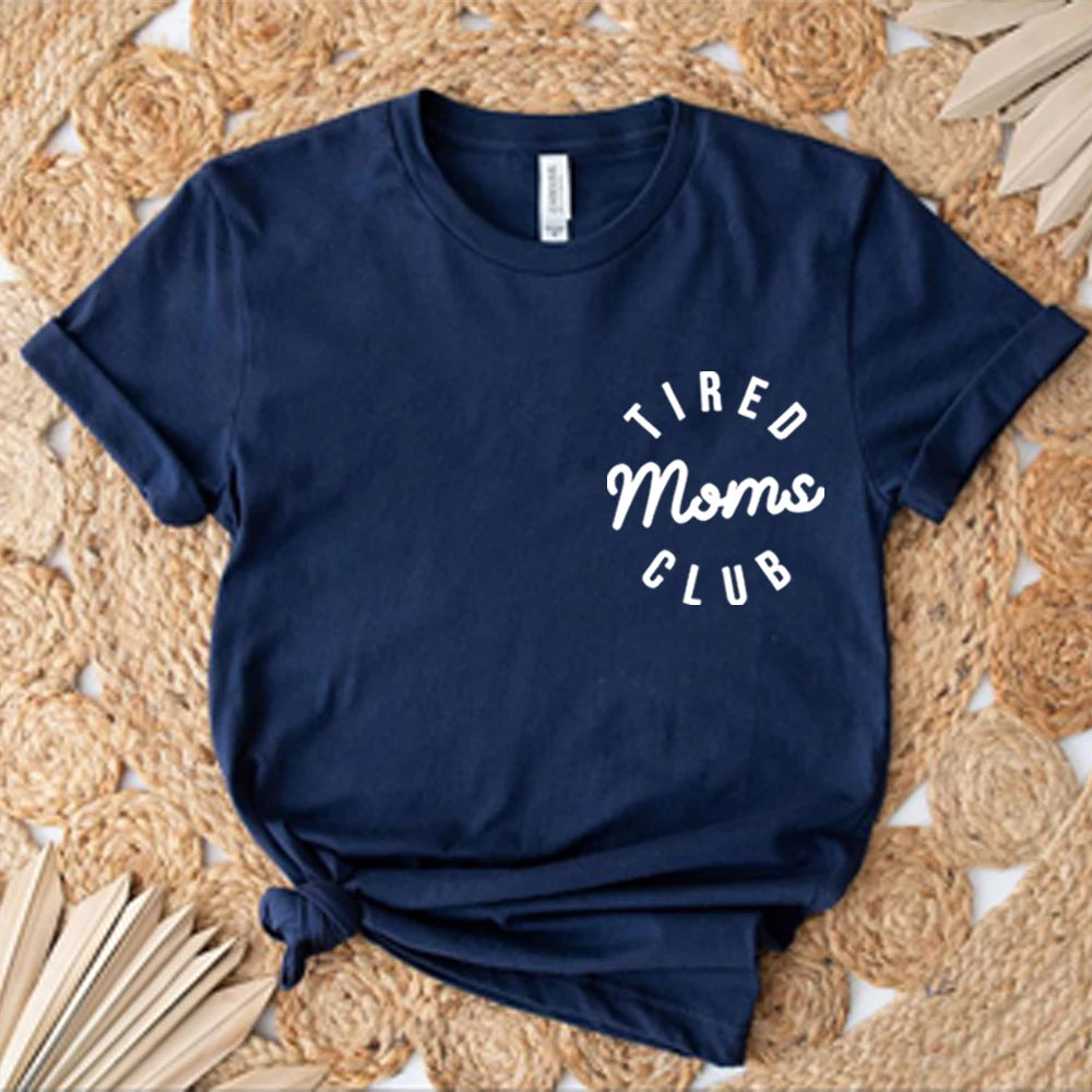 Navy blue t-shirt with 'Tired Moms Club' text on a woven mat background
