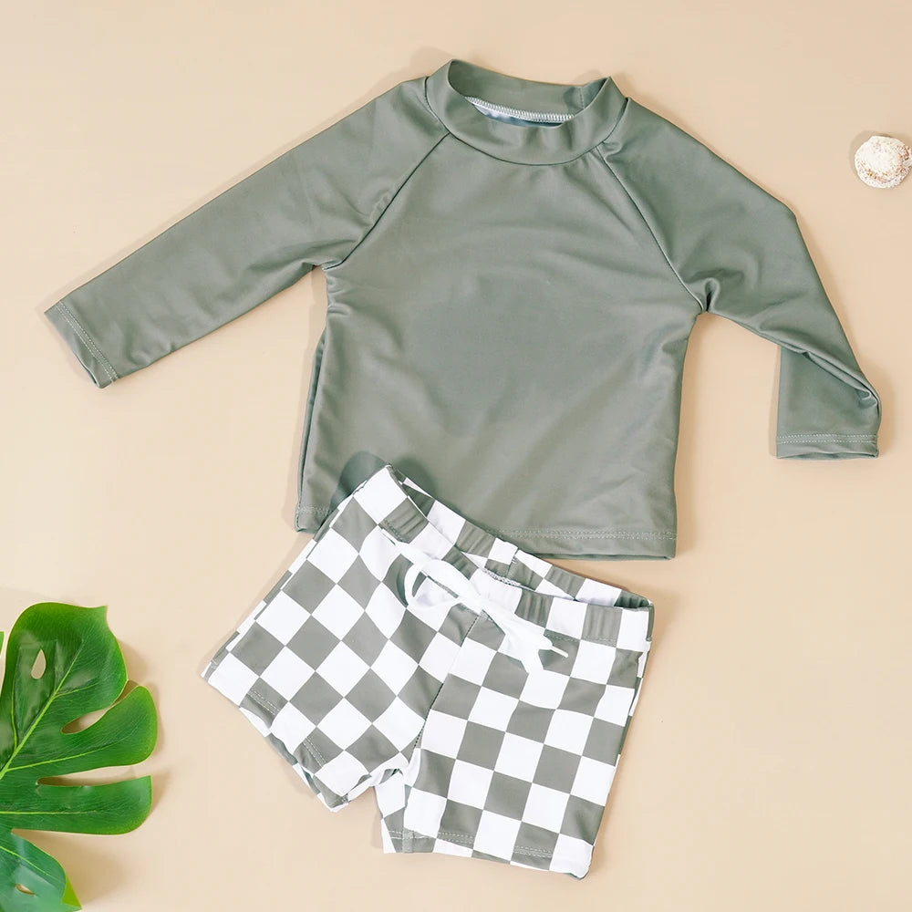 Green long-sleeve rash guard and checkered shorts on a beige background with a green leaf.