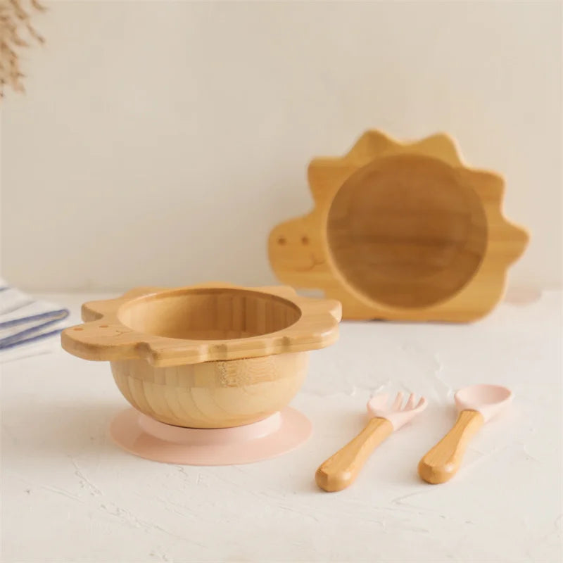 Wooden children's bowl, plate, and utensils on a light surface with a neutral background