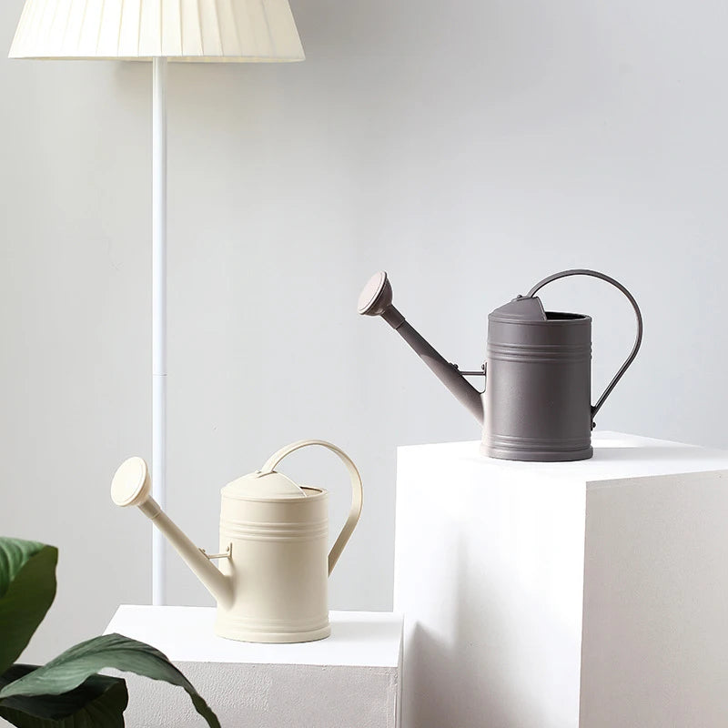 Two watering cans on a white surface with a light gray wall in the background.