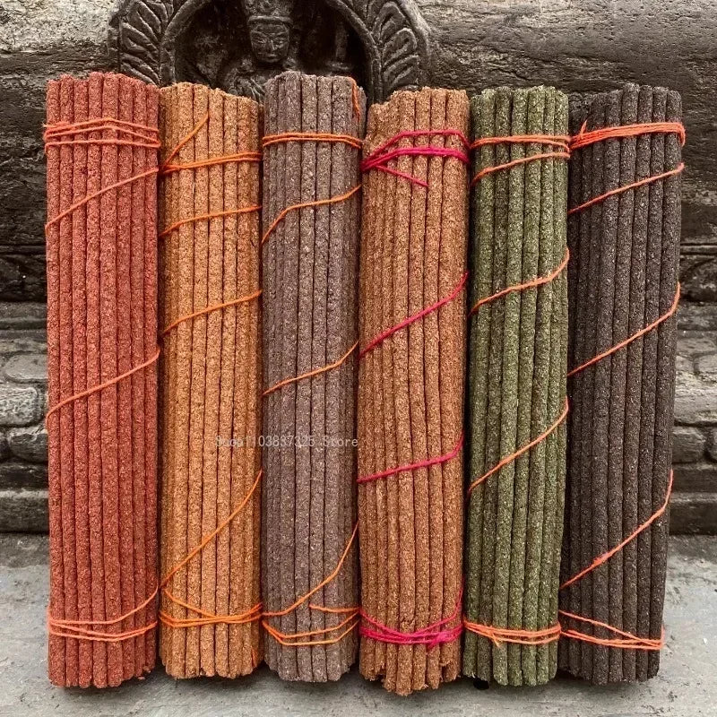 Set of six bundles of incense sticks in different colors tied with ribbons against a stone wall background.