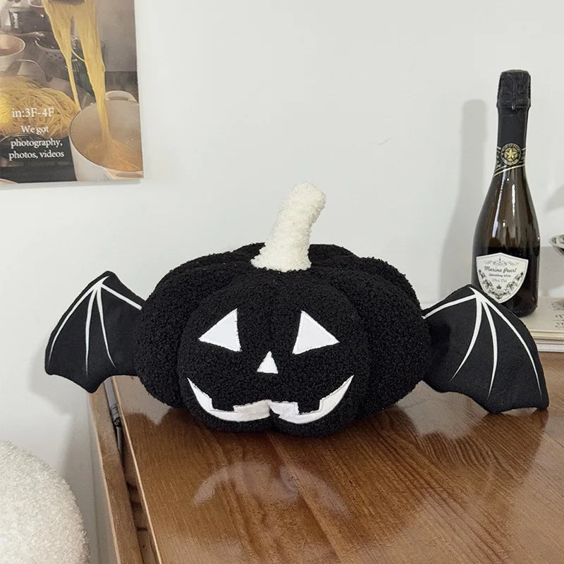 Black plush toy shaped like a jack-o'-lantern with bat wings on a wooden surface.