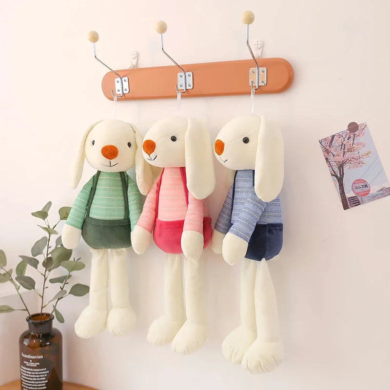 Three plush rabbit toys hanging on a wooden rod against a white wall.
