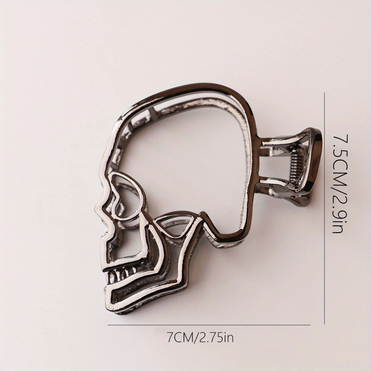 Metallic skull-shaped hair clip with measurements on a light background