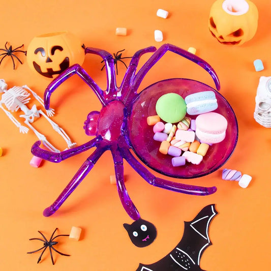 Halloween-themed purple spider candy dish with treats on an orange background