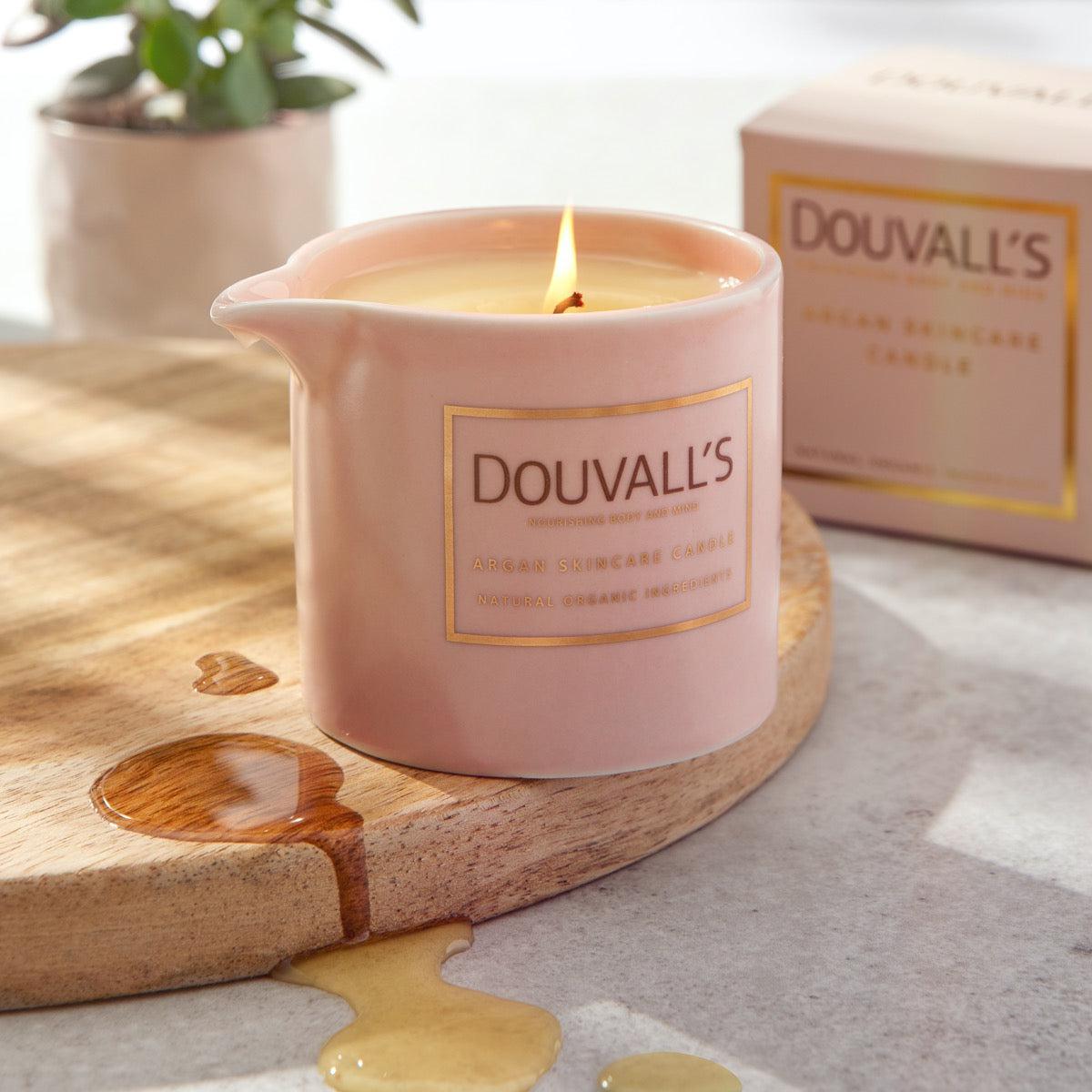 Pink Douvall's candle on a wooden coaster with packaging in the background