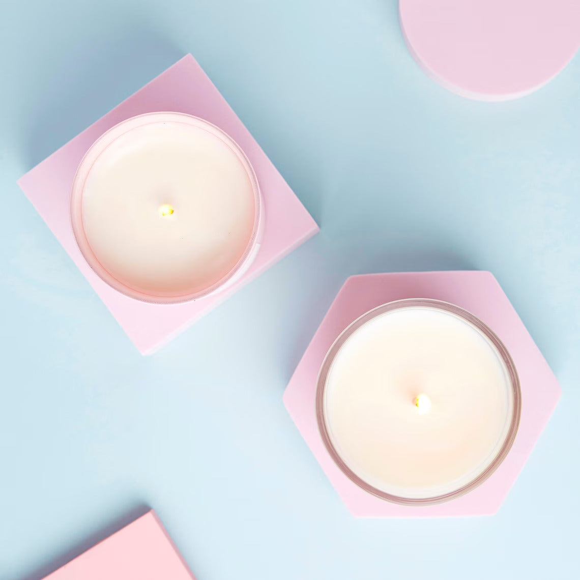 Two candles in pink holders on a light blue background
