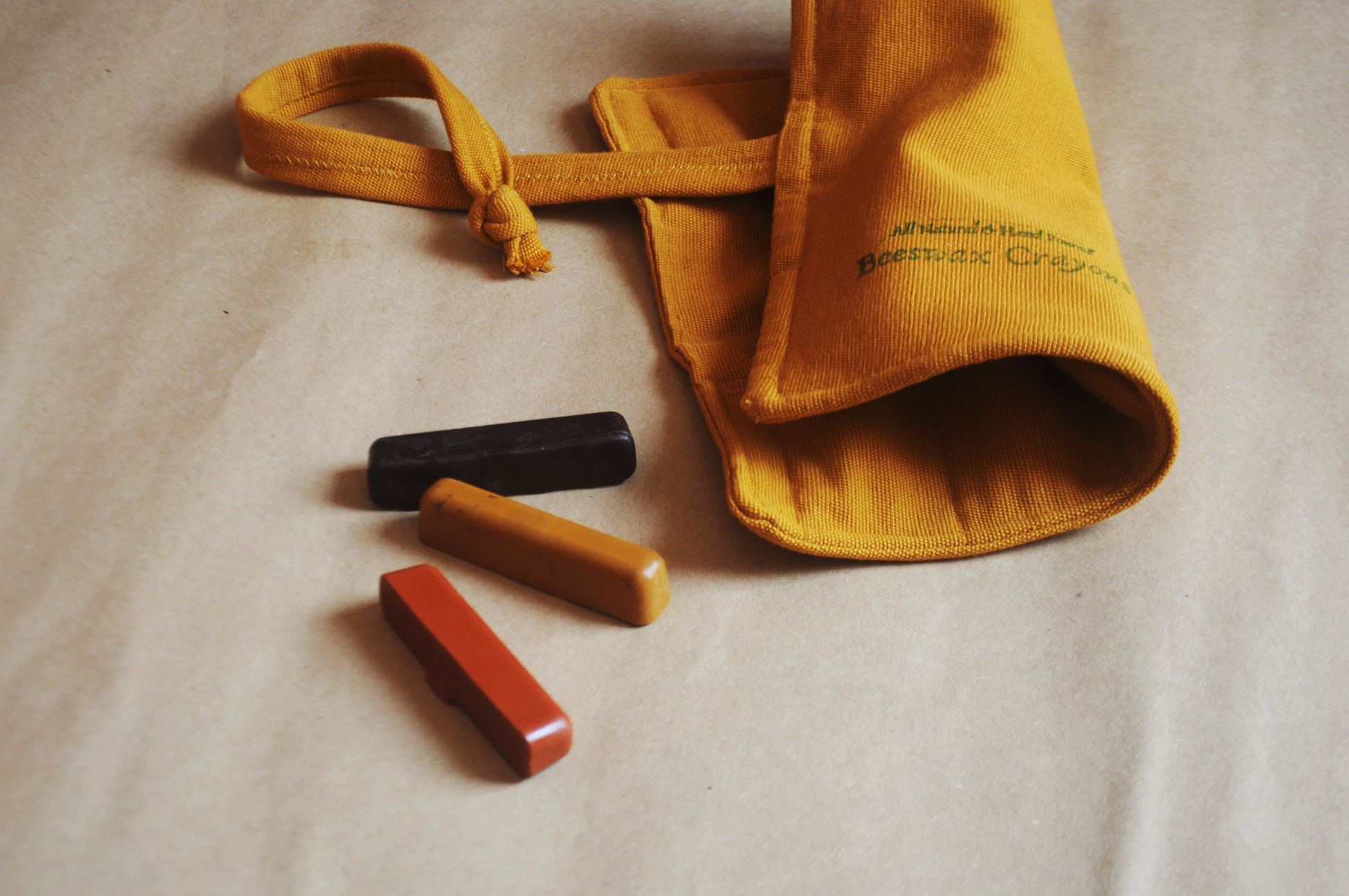 Yellow drawstring bag with three crayons on a beige surface