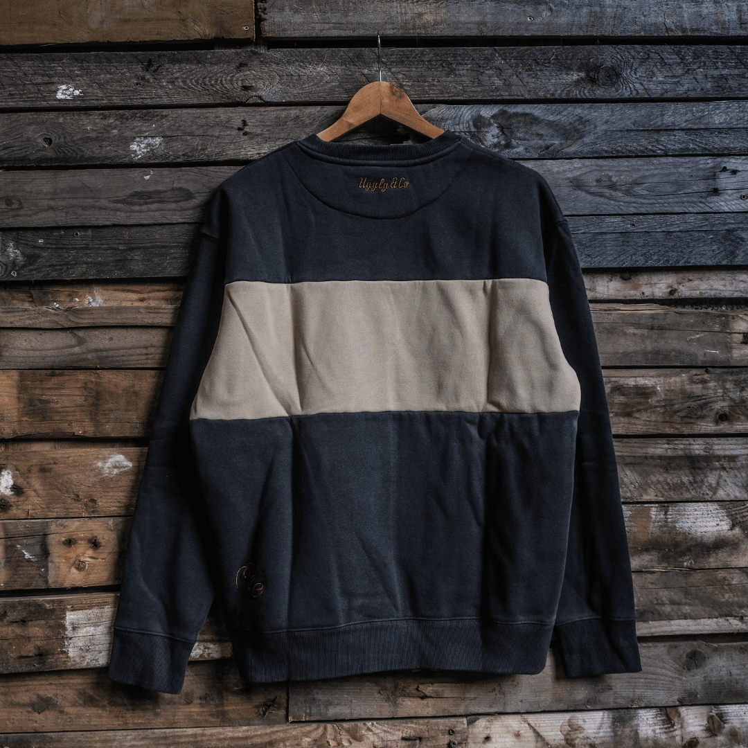 Two-tone black and beige sweatshirt hanging on a wooden hanger against a rustic wooden wall.