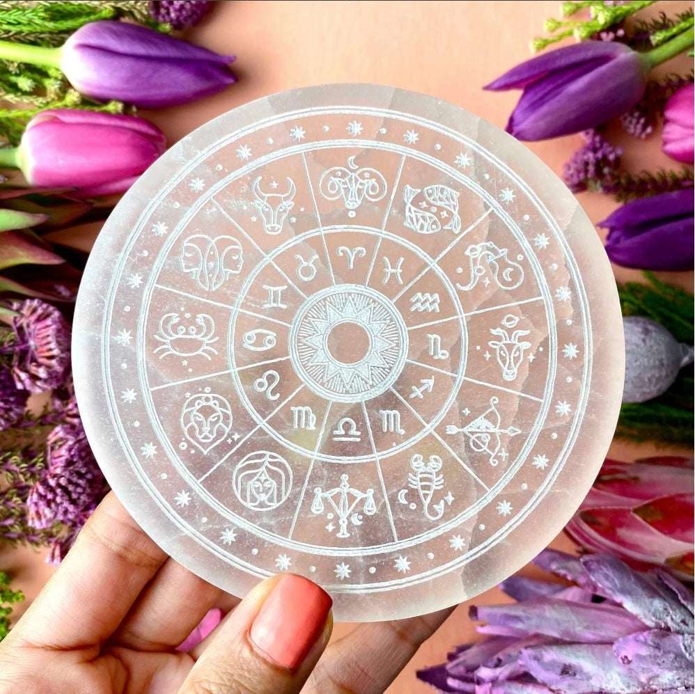 Circular sticker with zodiac symbols held over a background of purple flowers