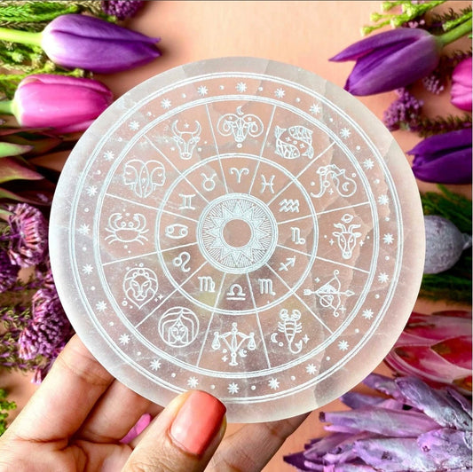 Circular sticker with zodiac symbols held over a background of purple flowers