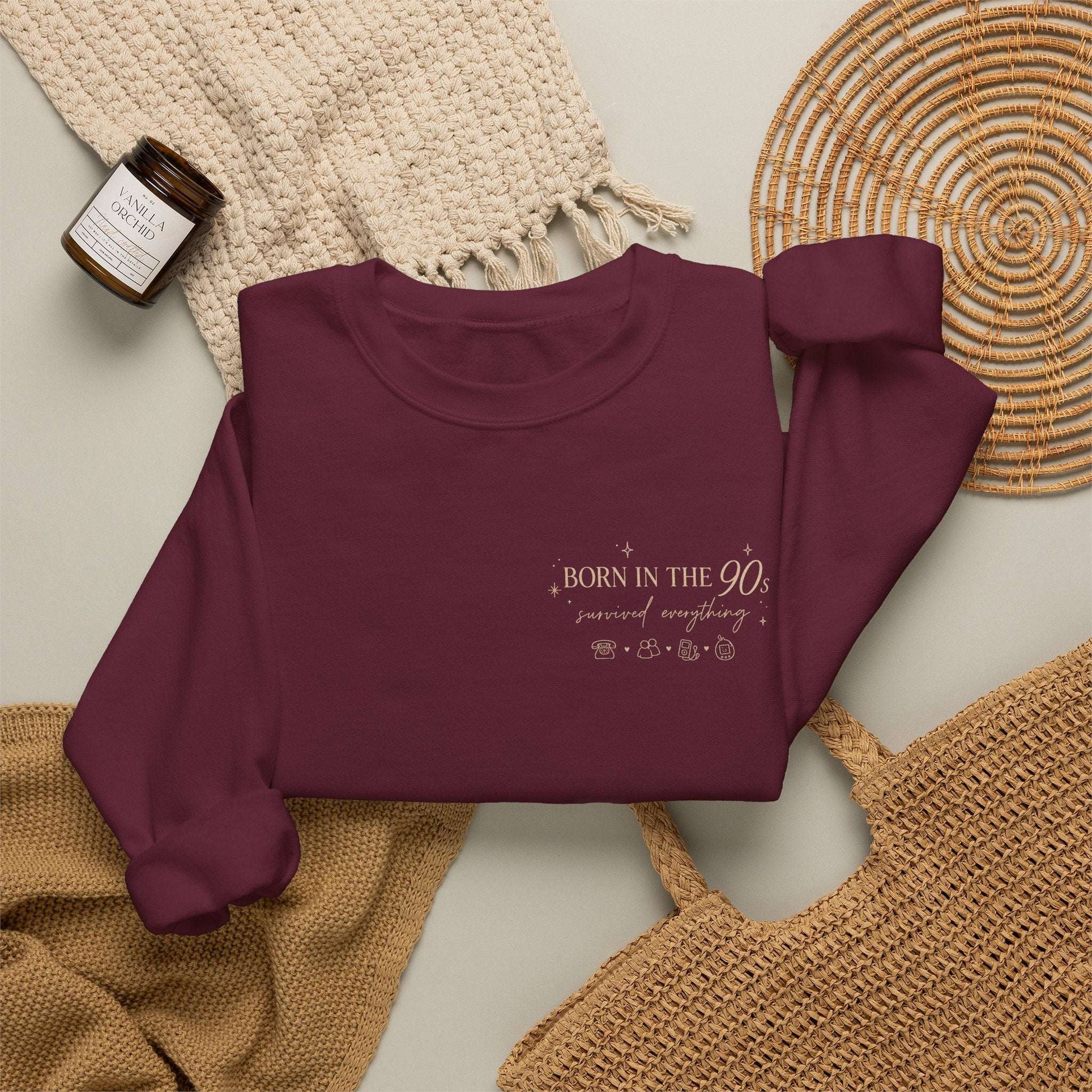 Maroon sweatshirt with 'Born in the 90s’ text on a textured surface 