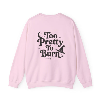 A light pink crewneck sweatshirt shown from the back, featuring a black graphic print that reads 'Too Pretty To Burn' alongside a small witch hat illustration.
