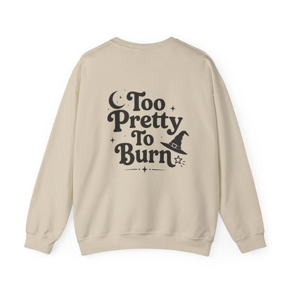 A beige crewneck sweatshirt shown from the back, featuring a black graphic print that reads 'Too Pretty To Burn' alongside a small witch hat illustration.