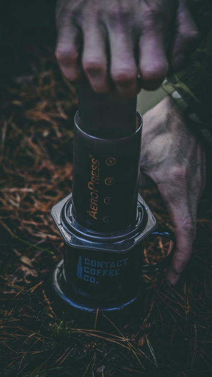A person holding a black AeroPress coffee maker on a natural background