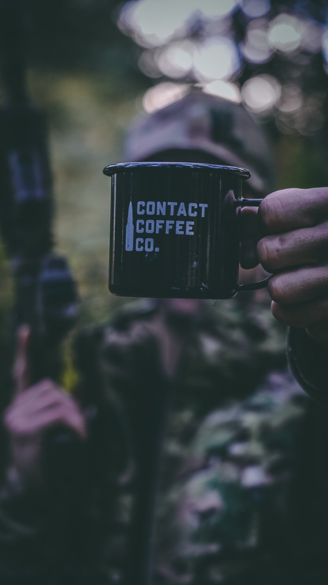 Person holding a black mug with 'Contact Coffee Co.' text against a blurred natural background