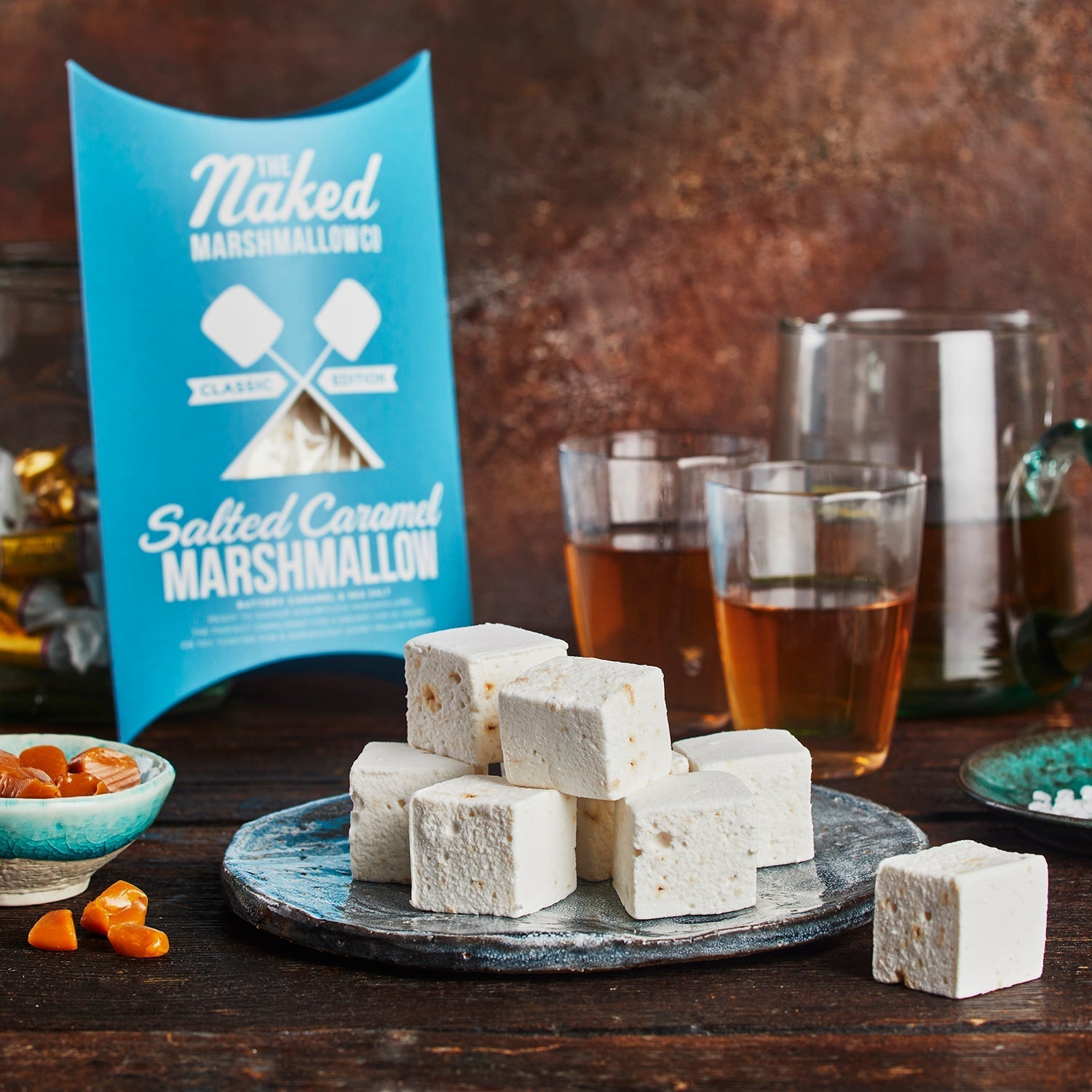 Salted caramel marshmallows on a plate with a 'The Naked Marshmallow' packaging and drinks in the background.