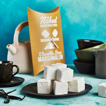 Naked Vanilla Bean Marshmallows on a plate with packaging and tea-making items in the background.