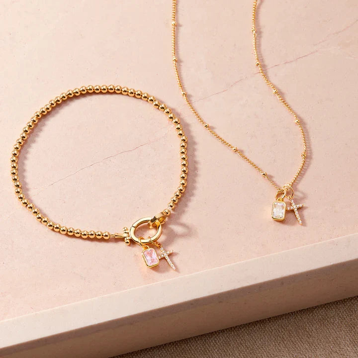 Gold bracelet and necklace with charms on a beige surface