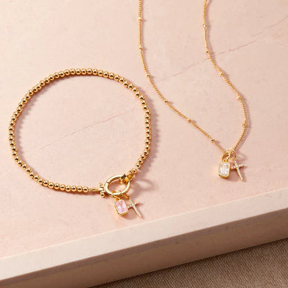 Gold bracelet and necklace with charms on a beige surface