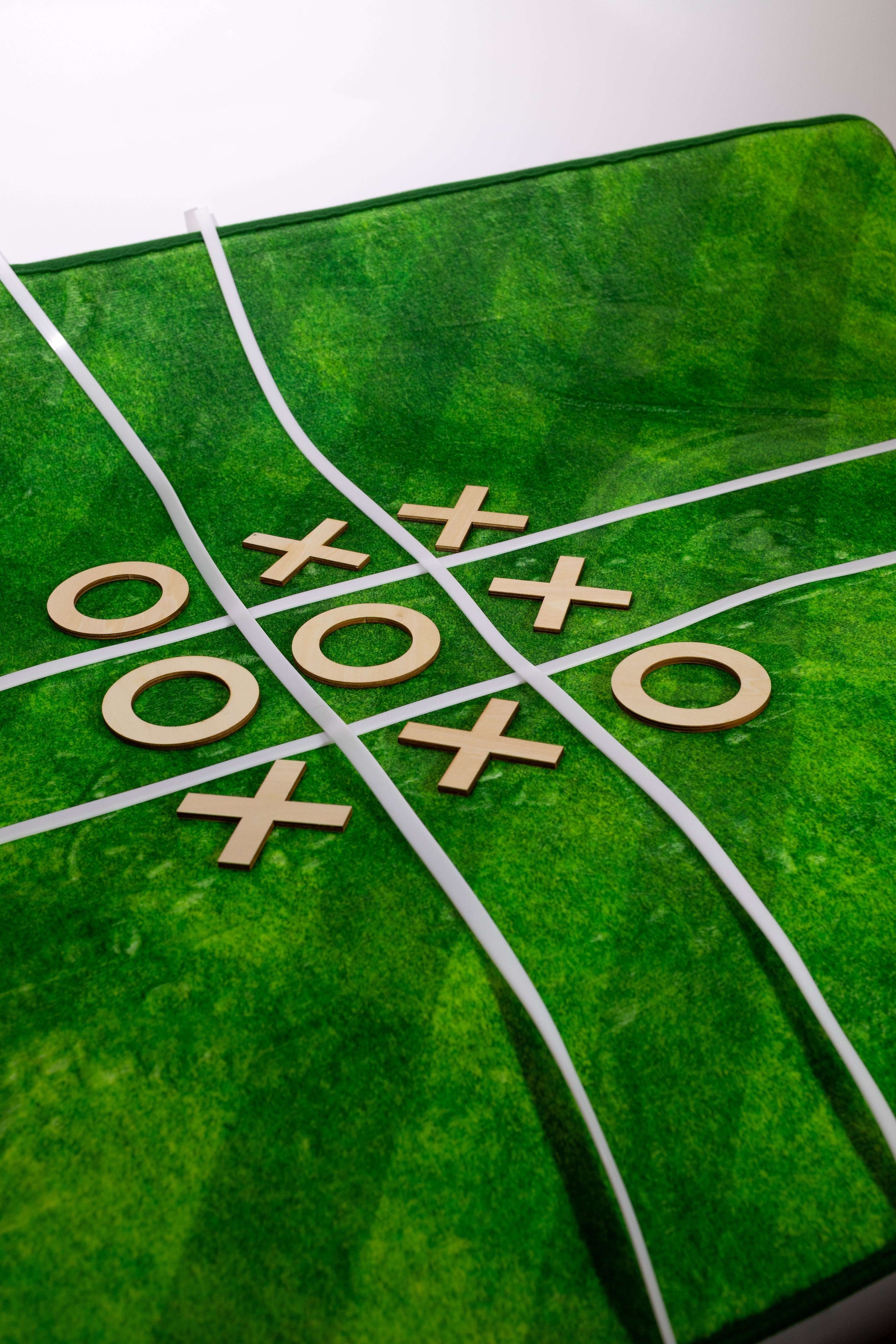 Green game board with tic-tac-toe pattern and wooden pieces on a white background